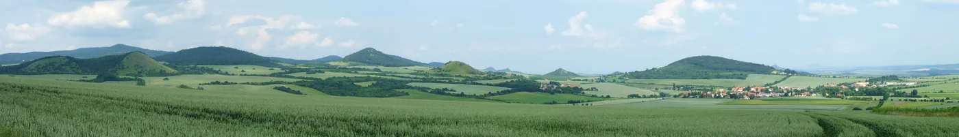 Panorama kuželovitých kopců nad poli a vesnicí